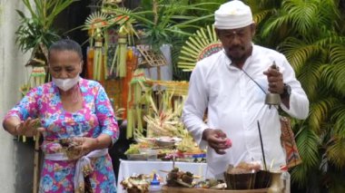 Ubud, Endonezya - 22 Ekim 2022: Bali ritüeli Şaman ve tören asistanı tarafından gerçekleştirilir. Bir Bali tapınağında, bir rahip yerel tören kıyafetleri içinde tanrılarına dua okur.