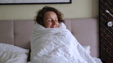 Düşünceli, kıvırcık saçlı, rahat beyaz battaniyeye sarılı genç bir kadın yatakta oturuyor. Sabah vakti, kışın soğuk ama rahat bir yatak odasında çalışmaya başlıyorum. Sabah uyanamayacak kadar tembelsin.