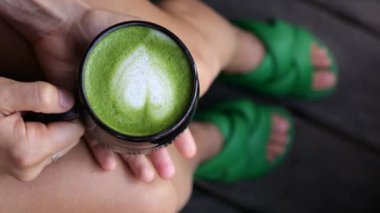 Evde oturan bir kadın elinde bir fincan sıcak kibritli latte tutuyor. Sıcak bir içecekle bütün gün koşuşturup rahatlıyor. Ev kavramı Bir fincan sıcak kibrit çayıyla sıcak bir an.