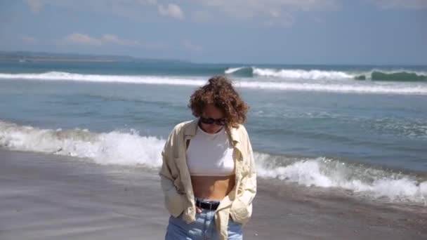 女人朝下看 沿着海滩散步 思考生命的意义 戴着太阳镜的卷曲女孩转向大海 思考生命的意义 散步有助于思考生命的意义 — 图库视频影像