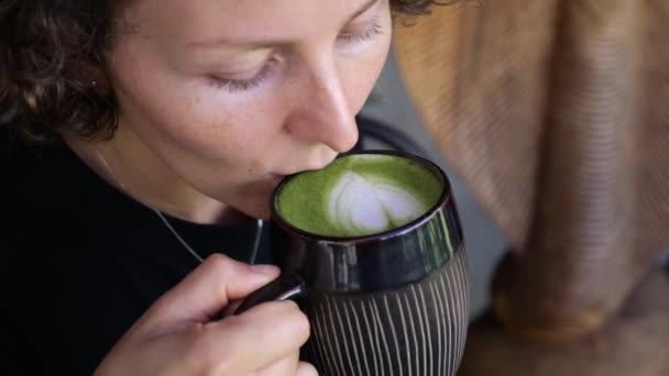 女性は熱い抹茶ラテを手に持ち 一日中熱い飲み物で喧騒から解放されます ホット抹茶を使った家庭的なコンセプトの居心地の良い瞬間 スローモーションビデオ — ストック動画