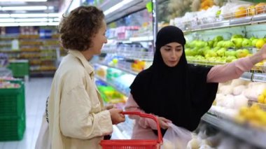 Farklı milletlerden iki genç kadın, bir süpermarkette meyve sergisinin yakınında canlı bir diyalog kuruyor. Tesettürlü bir kadın raftan bir armut ve limon alıp bir çantaya koyar.