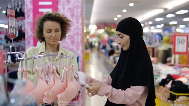 服装商店里不同种族和宗教的最好的朋友选择内裤和胸罩 在购物中心购物时 穿着头巾的白人和阿拉伯妇女选择内裤 — 图库视频影像