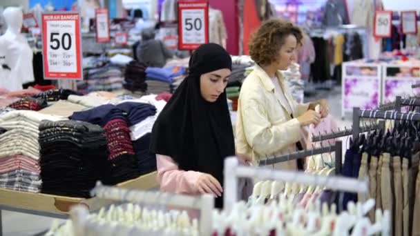 服装商店里的女顾客是为不同阶层的人服务的 穆斯林和白人妇女选择 看看衣服 查看分类 购买衣服 选择物品 作出购买决定 — 图库视频影像