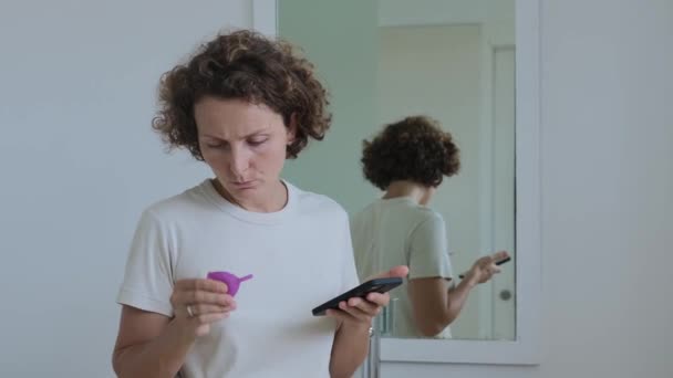女性は重要な女性の日に月経カップを使用する方法に関するインターネット上の指示を探しています 非環境衛生的なものに代わるシリコーン月経カップを使用する — ストック動画