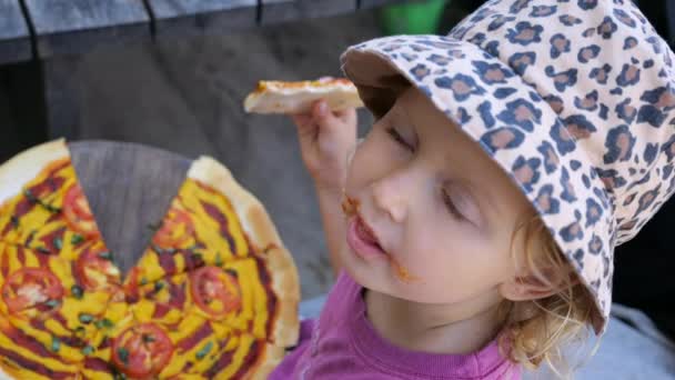 ピザを食べるキッズグルメのトップビュー 夏のカフェでトマトとチーズピザを楽しむ帽子でブロンドかわいい子供のシネマティックビデオ 子供の近くで 食べ物が汚れてる コンセプトはピザを食べる — ストック動画