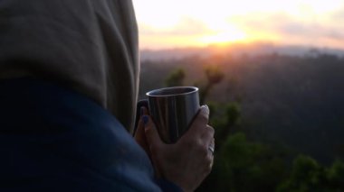 Genç bir kadın elinde bir kupa kahveyle dağlara tepeden bakan bir sis bulutuyla sabah yürüyüşçülerin yakın planında dağlardaki ormanların keyfini çıkarıyor.