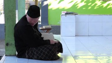Ubud, Endonezya - 22 Ekim 2022: Yaşlı Müslüman adam kutsal Kuran 'ı okur ve dua sırasında başını ona yaslar. Müslümanlar Kuran 'ı yüceltirler ve O' nu yüceltirler. Kuran okuyun, dua edin.