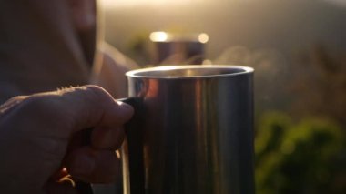 Kampta gezen bir çift, demir bardaklarda sıcak içeceklerin keyfini çıkarıyorlar. Vahşi doğada gündoğumunun sinematik videosu, sıcak içeceklerle birlikte dağ manzarası. Birlikte kamp kurup, sıcak içeceklerle birlikte yaşayın.