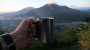 Sinema kameramanı, lüks dağ manzarasına karşı elinde buharlı demir bardak tutuyor. Kampta sıcak kahveyle gezgin bardağının yakın çekimi vahşi doğa kavramına dayanır. Kampa gidip demir kupanın içinde sıcak kahvenin tadını çıkarırız.