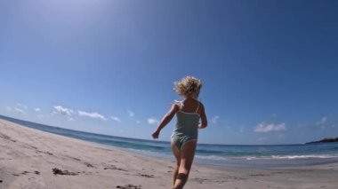 Balık gözü, yaz plajı boyunca koşan küçük kıza bakıyor. Güneşli bir günde okyanusa doğru koşan mayo giymiş güzel sarışın bir kız. Çocukların sağlıklı ayakları ve tüm vücudu için sahilde koşmalarına izin verme kavramı.