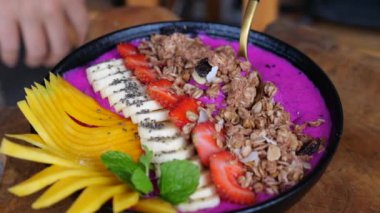Gurme, smoothie kasesinden vejetaryen smoothie kepçesini kaşıkla kapladı, yakın plan. Muz, ejderha meyvesi ve tahıllı taze meyve suyu kasesi. Yaz kafesinde sağlıklı vejetaryen yemekleri yemenin sinematik videosu..
