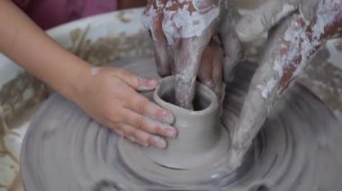 Anne ve çocuk çömlek çarkında kil çömlek yapıyorlar. Annelerin çocuklara rehberlik edip kilden tencereye hız kazandırdığı yakın plan. Kil çömlek yapıp güzel anılar yaratırken ailenle vakit geçirme kavramı.. 