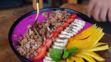 Gurme bir kaşık dolusu smoothie kasesi yakına çekiyor. Gurmeler muz, ejderha meyvesi ve tahılla besleniyor. Gurme ziyafetinin sinematik videosu, yemek severler için lezzet ziyafeti. Sağlıklı beslenme kavramı.