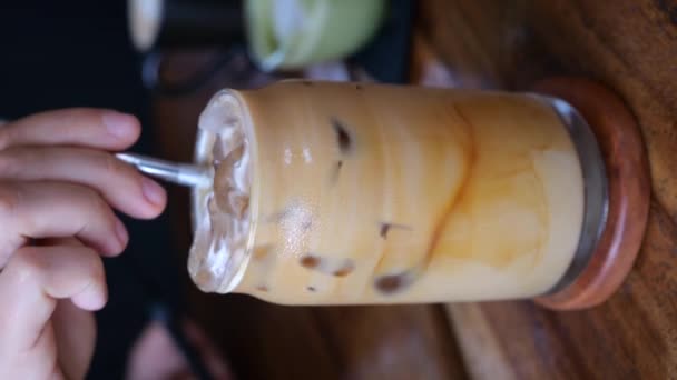 コーヒー愛好家は メタルストロー 垂直ビデオでアイスコーヒーをかき混ぜます 居心地の良いカフェの設定でアイスコーヒーのシネマティックビデオ アイスコーヒーの爽やかな飲み物の完璧な一杯をお楽しみください — ストック動画