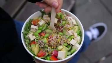 Lezzetli yemek tabağı içeren gurme yakın çekim. Avokado parçalarını, lahanaları, bezelyeleri, domatesleri çatalla karıştıran bir kadının sinematik videosu. Paket yemeğin tadını çıkarıyorum.