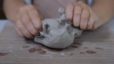 Bir çocuk çömlekçilik kursunda kil şekillendirir. Çocuksu ellere yakın çekim ve şekil verebilmek için nemlendirilmiş kil. Çocukların kendi kil bardaklarını yapmaları, yoğurmaları ve atölyede kille çalışmaları.