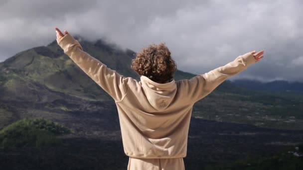 空に手を上げて自由を感じる美しい山に対する女性のリアビュー 山の自由感のシネマティックビデオ 自然の美しさを見るコンセプト旅行 山で自由の喜びを感じる — ストック動画