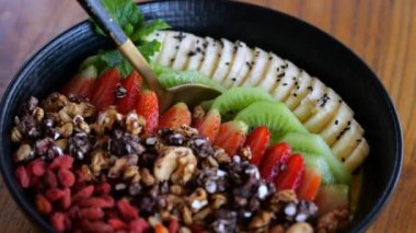 Kaşık kepçeli gurme meyve suyu kasesinden vejetaryen yemeği kaşıkla yakın plan. Muzlu, kivili, goji üzümlü taze vejetaryen yemeği sineması. Yaz kafeteryasında sağlıklı vejetaryen yemeğinin tadını çıkarma kavramı.