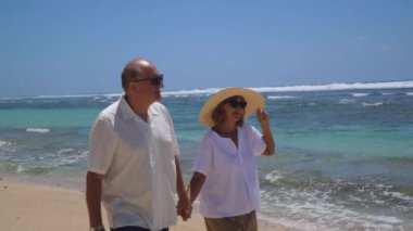 Güneşli okyanus sahillerinde yaşlı çiftin romantik yürüyüşü. Kadın ve erkek sahilde mutlu zaman geçiriyorlar. Plaj ve deniz manzarasının güzelliğine karşı ilişki uyumu kavramı