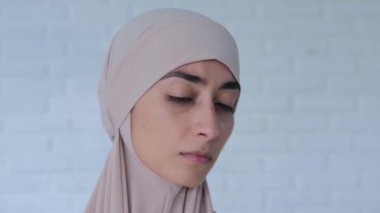 Başörtülü Müslüman kadın üzgün bir şekilde kameraya bakıyor. Güzel yüz hatları, sabit bakışlar ve ciddi bakışlar insanı gerer. Bu görüntünün kelimelerden çok daha fazla duygu ifade ettiğini kabul et..