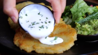 Gurme patatesli krep üzerine baharatlı ekşi krema sosu döker, yakın plan. Lezzetli patates kreplerinin, sosun, restoranda salatanın sinematik videosu. Kahvaltıda patatesli krep yeme kavramı