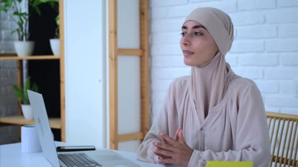 穿着头巾坐在办公室里的有魅力的女人 在工作中思考着新的商业理念 在笔记本电脑旁舒适的办公室里 一位穆斯林女士因商业理念而情绪高涨 商业理念概念 — 图库视频影像