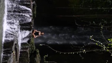 Meditasyonda şelalede güç toplayan bir kadının dikey videosu. Heyecan verici bir video: Düşen suyun gücü Şelale 'deki gücünüzü yeniden oluşturmaya yardımcı olur 