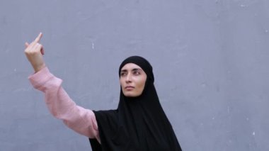 Tesettürlü güzel bir doğulu kadın el ele tutuşarak saldırgan bir hareket sergiliyor. Müslüman kadın, Doğulu kadınlara karşı saygısız ve kaba tutumu protesto ediyor. Orta parmak protesto işareti olarak