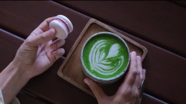 Sıcak kahve dükkanında makarna ve sağlıklı bir kibrit. Zarif eller dikkatli bir şekilde nefis bir tatlı ve aromatik bir içecek tutar. Kahve dükkanları, pastaneler, tatlılarla ilgili bloglar için sinematik çerçeve