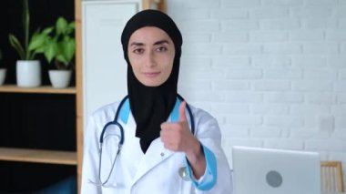 Tesettürlü, üniformalı ve steteskoplu Müslüman bir kadın doktor baş parmak işareti gösteriyor. Doktorlar jesti onaylıyor, olayların olumlu sonucunu gösteriyor ve hasta jestlerinin kelimelerden daha anlamlı olmasını teşvik ediyor.