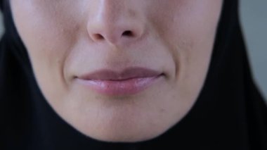 Gülümseyen Müslüman kadın dudaklarını kapat. Siyah tesettürlü, güzel tombul dudaklı, kameraya gülümseyen Müslüman kadının sinematik videosu. Kişisel mutluluğunuzu gülümseyen ve ilham veren bir şey olarak görün.