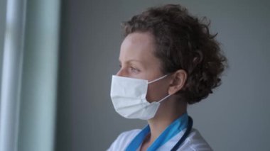 Tıbbi maskeli ciddi bir doktor hastanenin penceresinden dışarı bakar. Doktorlar yoğun tıbbi çalışmaların karmaşıklığı hakkında düşüncelere işkence ettiler. Görünüşte tıbbi alanda daha iyi bir gelecek için derin bir umut ortaya koyuyor.