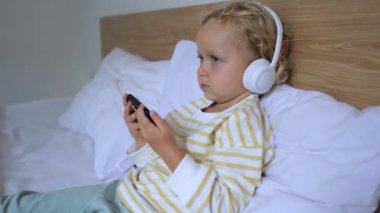 Akıllı kız telefondan kulaklık kullanarak sesli kitap ya da eğitim materyali dinliyor. Cihazların yardımıyla eğitim biçimi modern çocuklar için önemlidir. En sevdiği alet üzerinde çocuk eğitimi.