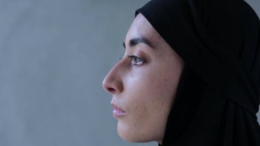 Siyah tesettürde özenle duran Müslüman bir kadının portresi. Profil Müslümanının yakın çekimi sakince duruyor ve uzaklığa bakıyor. Profilde ayakta duran bir kadının güzel yüz hatları
