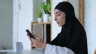 Başörtüsü içindeki Arap kadın yere bakar ve cep telefonlarıyla sohbet eder. Cep telefonlarında yazışmalar yoluyla modern iletişim kavramının ayrılmaz bir parçası haline gelmiştir..