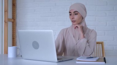 Başörtüsü takan serbest çalışan evde rahat bir şekilde oturuyor ve işini internetten yapıyor. Serbest çalışmak her zaman ve her yerde mümkün olmuştur. Müslüman kadın serbest çalışanın sinematik çekimi..