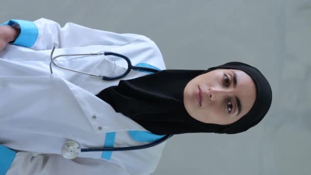 穆斯林女医生头戴头巾和制服与听诊器穆斯林医生的垂直录像在现代诊所的办公室里工作 医生自信的样子表明他的专业水平和对自己领域的了解 — 图库视频影像
