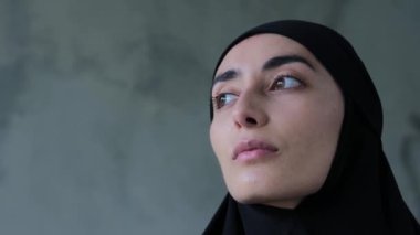 Müslüman kadın kameraya ciddi bir ifadeyle bakıyor. Yakın plan, alttaki bakış: Müslüman kadın hayalindeki mesafeye bakar, sonra kameraya bakar. Konsept: Müslüman kadın kameraya bakıyor