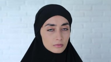 Siyah tesettürlü Müslüman kadın kameraya bakıyor. Yakın plan: siyah tesettürlü Müslüman kadın yüzü - güzel kahverengi gözler, şehvetli dudaklar, zarif oval yüz. Müslüman kadının klasik güzelliği.