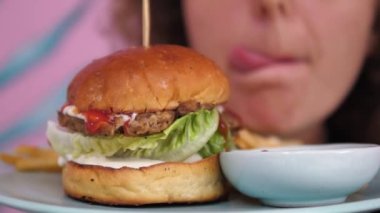 Burger ve gurme, seçici odaklanma. Patates kızartmalı ve soslu hamburgerin hemen arkasında dudaklarını yalayan gurme bir kadın var. Kavram: Acıktığın zaman en iyi çözüm hamburgerdir.