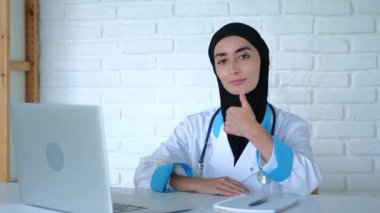 Müslüman kadın doktor onay ve anlaşma olarak onay verdi. Yakın plan çekim: Tıp önlüğü ve siyah tesettürlü Müslüman kadın doktor baş parmak hareketi kavramını onaylama ve anlaşma olarak gösteriyor