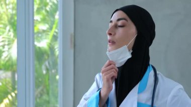 Penceredeki Müslüman kadın doktor tıbbi maskeyi çıkarıp tapınağı ovuyor. Siyah tesettürlü Müslüman kadın doktor iç geçirir, tıbbi maskesini çıkarır ve yorucu bir şekilde tapınağı ovalar. Yorgun doktorun dinlenmesi gerekiyor.