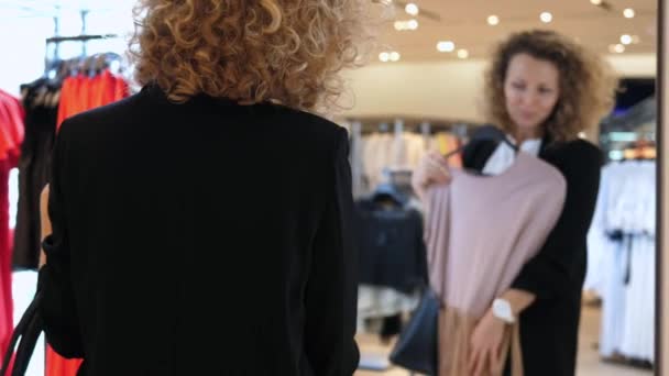 服装店的企业家从新系列服装中挑选时髦服装 女人在镜子中仔细审视她的衣服 办公室职员想买一套新衣服来代替下班后穿的西装 — 图库视频影像