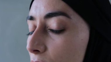 Siyah tesettürlü Müslüman kadının yüzü dönüp kameraya bakıyor. Yakın plan: Müslüman kadının düşünceli yüzü, gözleri tamamen açık. Kavram: Müslüman kadın kınayıcı bir bakışla karşı karşıya