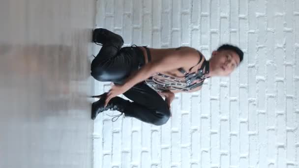垂直ビデオ カメラでポーズをとる同性愛者は カメラを見ているラテックスベルトゲイで作られた革のスーツに木製の床に横たわっています コンセプトLgbtコミュニティ 流行の流行のダンスの多様性 — ストック動画