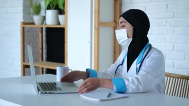 Laptopta yazan Müslüman kadın doktor. Yakın çekim: Müslüman kadın doktor dizüstü bilgisayarını hareket ettiriyor ve klavye üzerinde çalışıyor. Konsept: dizüstü bilgisayar doktorların belgeleri tutmasına yardımcı olur