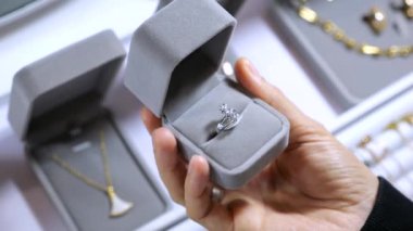 Kutuda gümüş bir yüzük var. Yakın plan: Alıcının halkayı döndürme görüntüsü, her yönden ona bakıyor. Şık gri kutu avucunun içine rahatça sığar. Konsept: Mücevher mağazasından yüzük almak