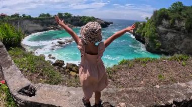 Gök mavisi suyu olan küçük bir tropikal koy. Geniş açı: küçük kız uçurumun kenarında duruyor ve Rocky Bay 'e hayran, kolları açık, uçmayı hayal ediyor. Konsept: tropikal körfez - hayalperestler için harika bir yer