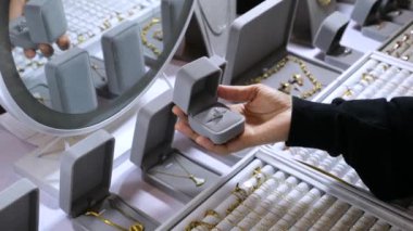 Kutuda gümüş bir yüzük var. Ortalama çekim: Alıcı, her yönden ona bakarak halkayı çevirir. Masada mücevherlerle dolu açık kutular var. Zincirler, kolyeler, yüzükler. Konsept: butikten mücevher almak